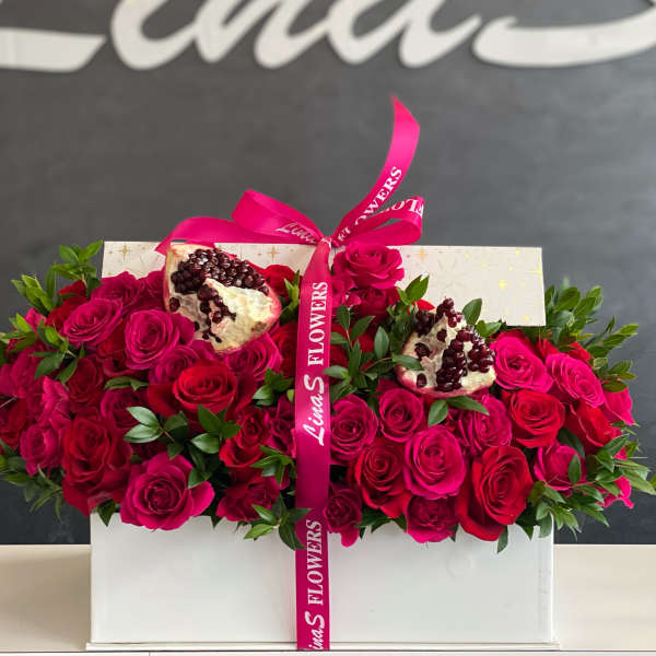 Box of hot pink and red roses with pomegranate halves and a pink ribbon