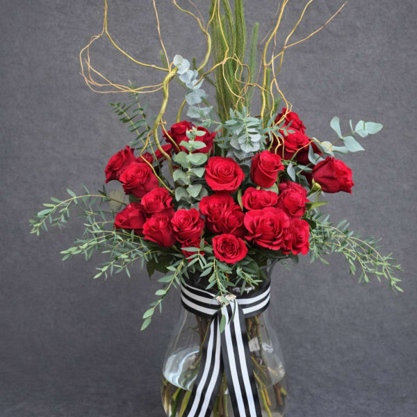 Red roses in a clear glass vase with black-and-white ribbon