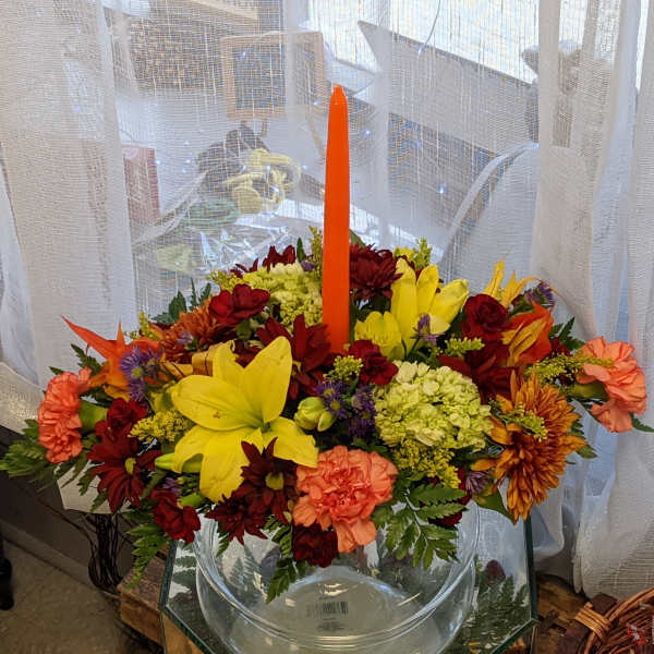 Colorful floral arrangement in a clear glass bowl with a tall orange candle