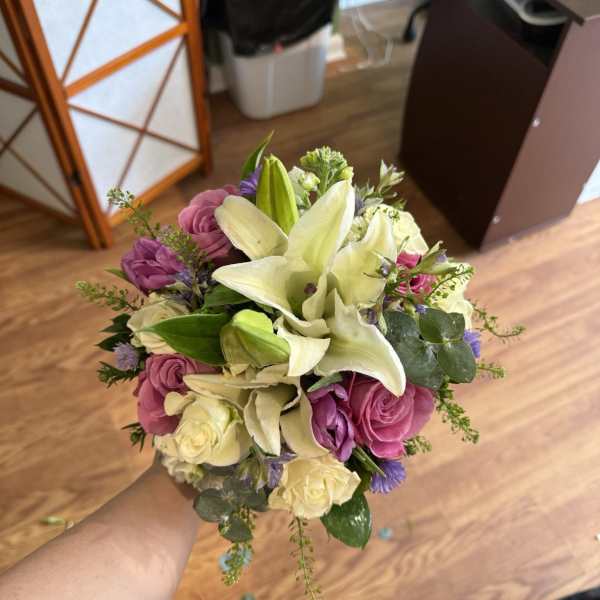 Handheld bouquet of white lilies, pink roses, and purple flowers