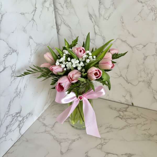 Pink tulips and white filler flowers in a glass vase with a pink ribbon