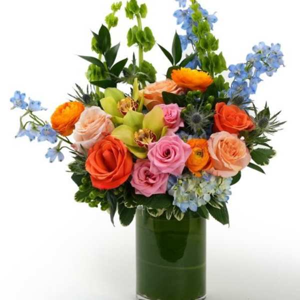 Bright mixed bouquet of roses, orchids, and hydrangea in a clear glass cylinder vase