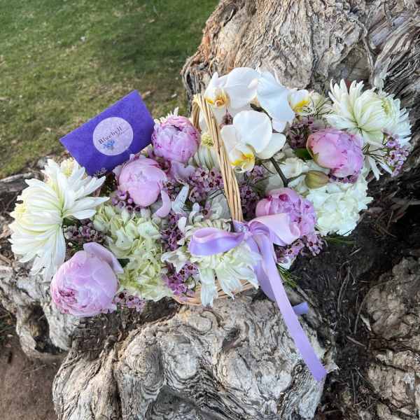 Basket of pink and white flowers with a lavender ribbon outdoors