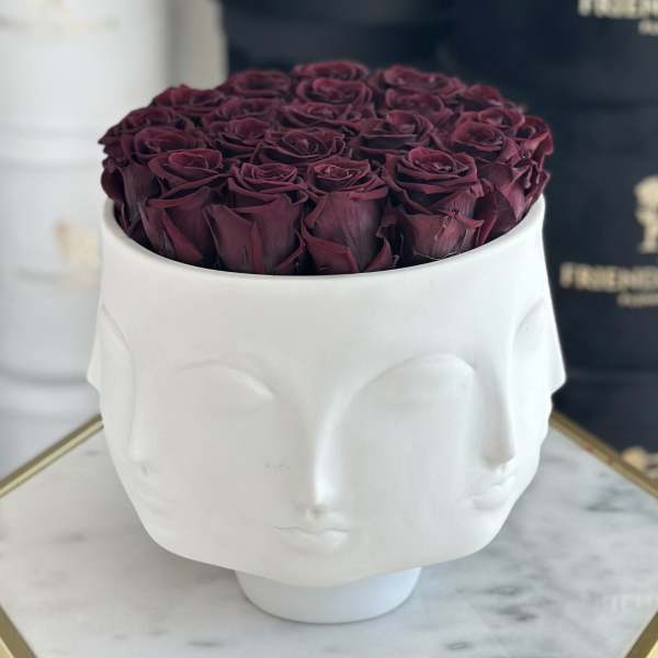 Deep burgundy roses arranged in a white sculptural face vase