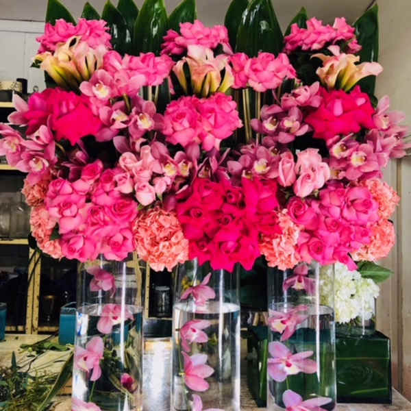 Pink floral arrangements in tall glass cylinders with orchids and roses