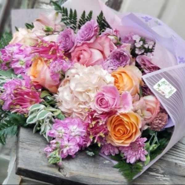 Bouquet of pink, peach, and lavender flowers wrapped in pale purple paper