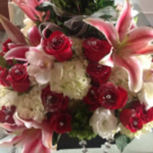 Red roses, pink lilies, and white hydrangeas arranged in a jeweled centerpiece-style floral design
