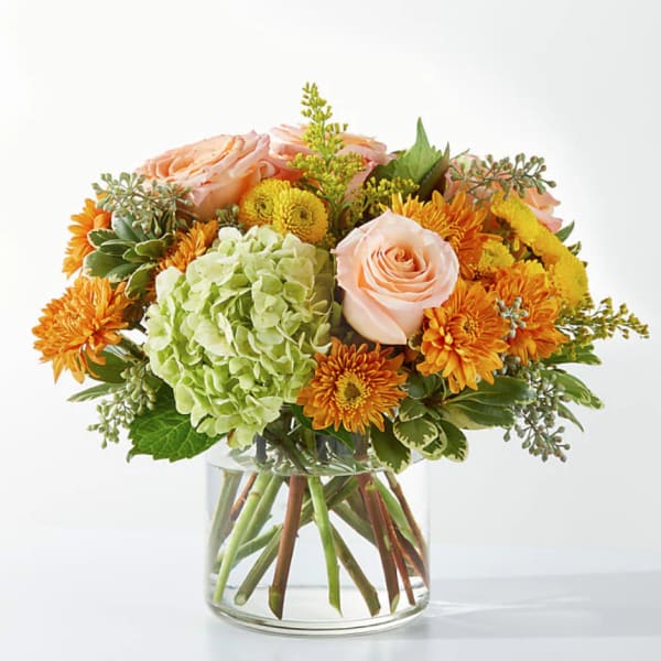 Peach roses and orange mums in a clear glass vase with green hydrangea