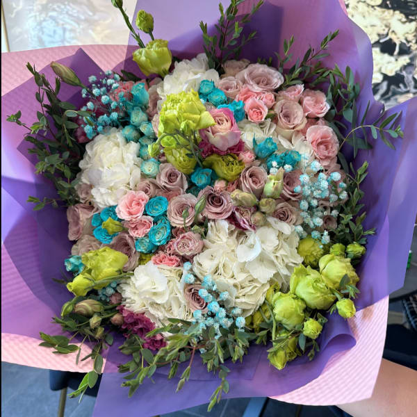 Bouquet of pastel roses, hydrangeas, and green lisianthus wrapped in purple paper