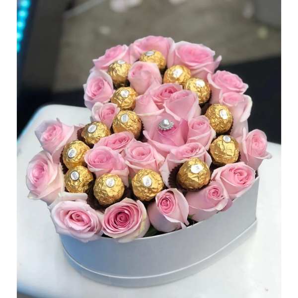 Pink roses arranged with gold-wrapped chocolates in a round box