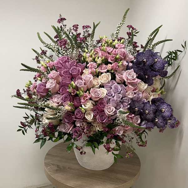 Large arrangement of pink and lavender roses with purple orchids in a white pot on a table