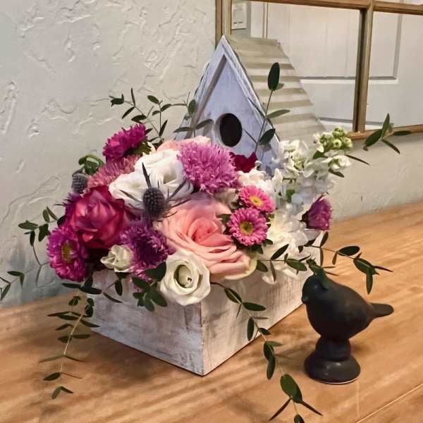 Pink and white floral arrangement in a birdhouse-shaped container