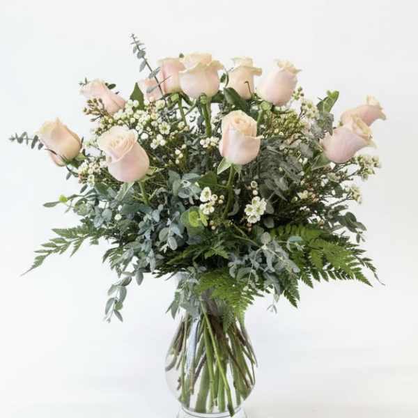 Blush pink roses in a clear glass vase with mixed greenery