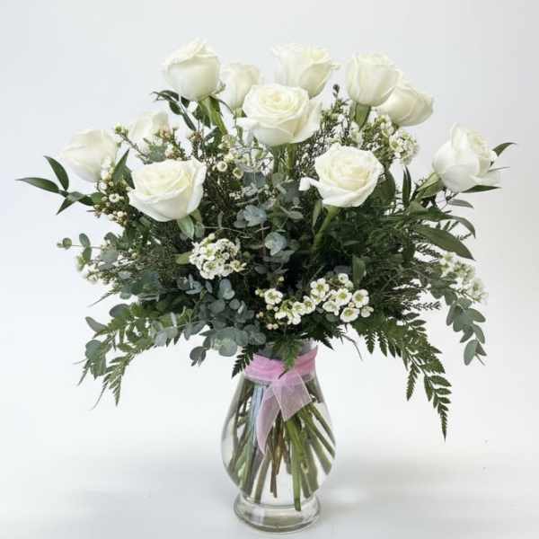 White roses in a clear glass vase with mixed greenery