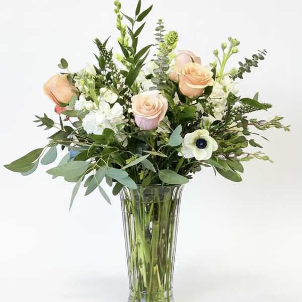 Peach and white roses in a clear glass vase with mixed greenery