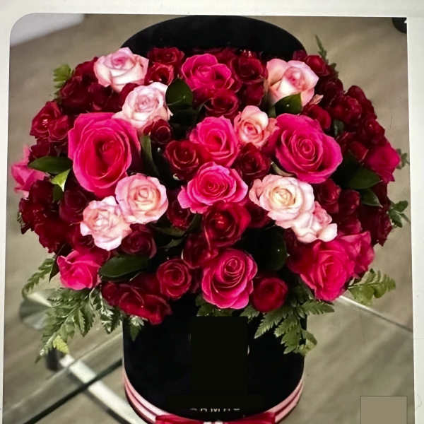 Round bouquet of pink and red roses in a black hatbox with a ribbon