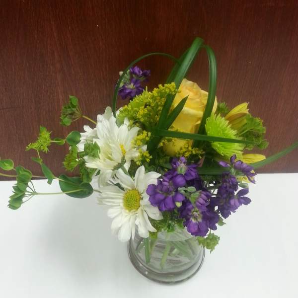 Bouquet of white daisies, yellow roses, and purple flowers in a glass vase