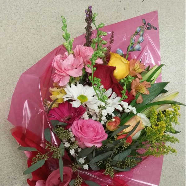 Mixed bouquet of pink, red, yellow, and white flowers wrapped in pink paper
