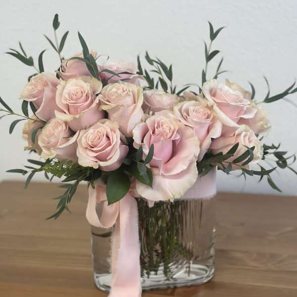 Pink roses arranged in a clear glass vase with a pink ribbon