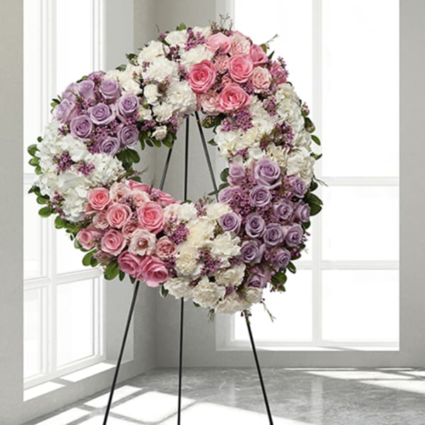 Heart-shaped floral wreath on a stand with pink, lavender, and white roses
