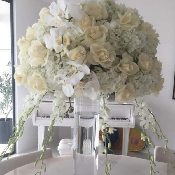White floral arrangement in a clear glass vase with trailing orchids