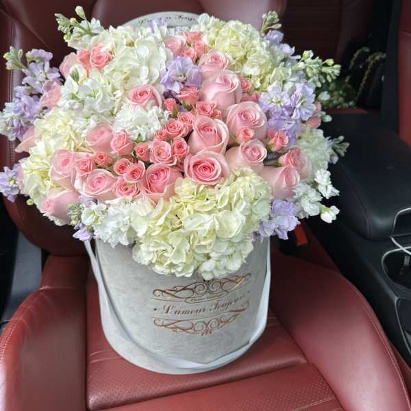 Round hatbox arrangement of pink roses, white hydrangeas, and pastel flowers on a car seat