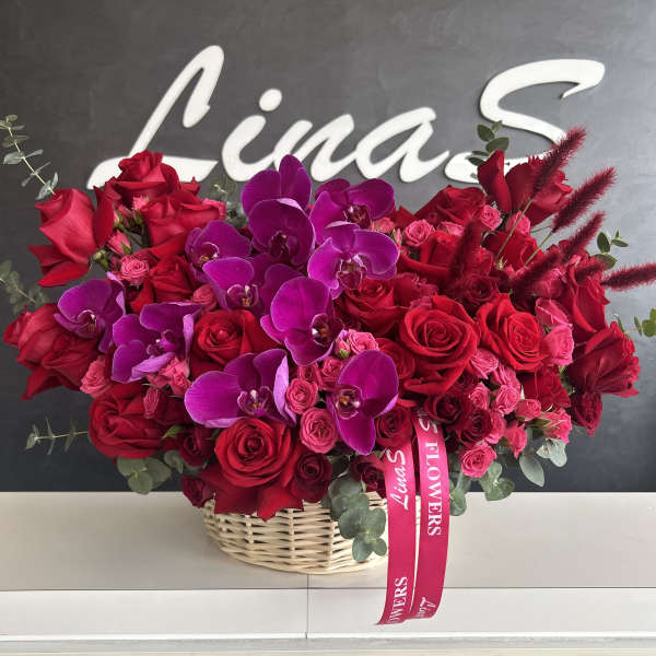 Basket arrangement of red roses and purple orchids with pink ribbon