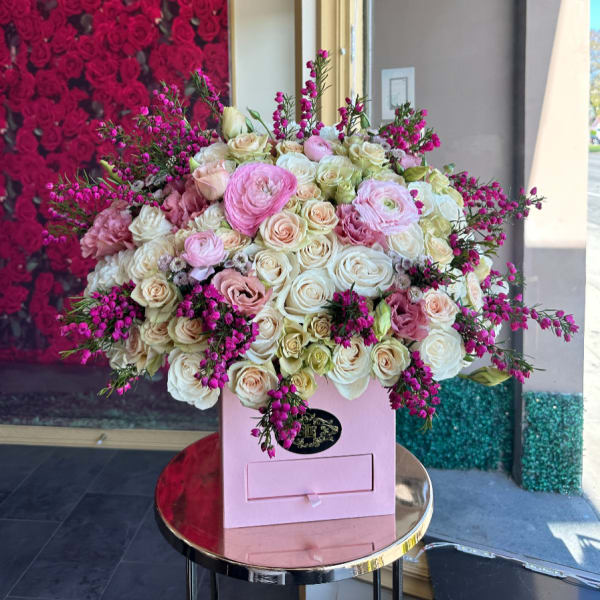 Lush arrangement of pink and cream roses and ranunculus in a pink hat box on a small round table