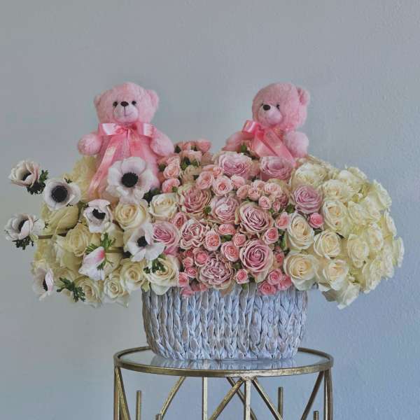 Pink teddy bears above a basket of pink and cream roses and anemones
