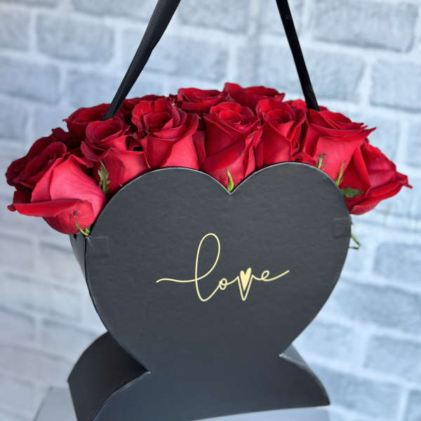 Red roses in a black heart-shaped box with a "love" label
