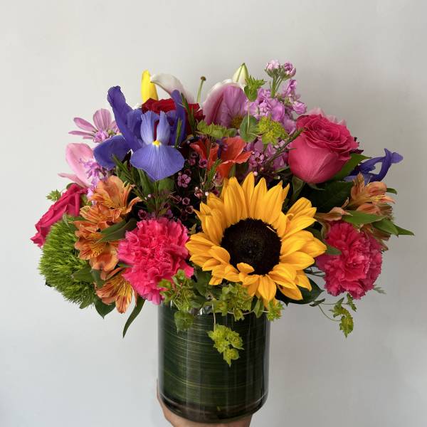 Mixed bouquet with a sunflower, roses, iris, and pink carnations in a glass vase