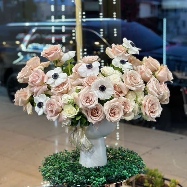 Blush roses and white anemones arranged in a white pedestal vase