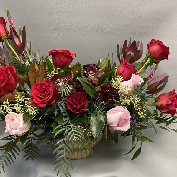 Red and pink roses arranged in a low basket with mixed foliage