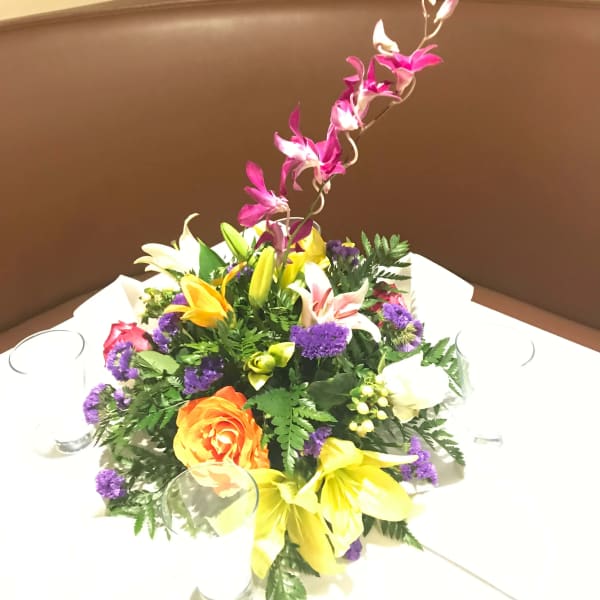 Colorful floral centerpiece in a low arrangement with a tall orchid stem