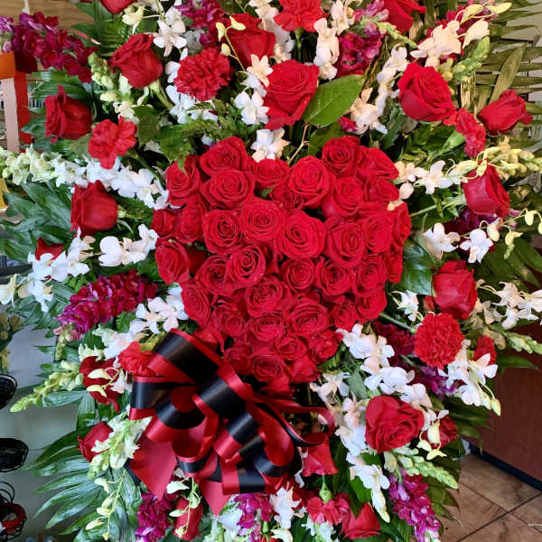Large red rose and orchid standing spray with a black-and-red ribbon bow