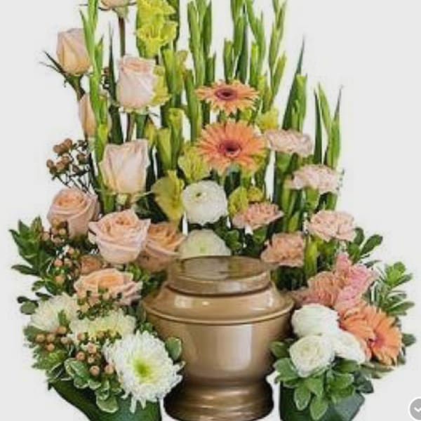 Tall floral arrangement with peach roses, gerbera daisies, and white blooms in a bronze urn