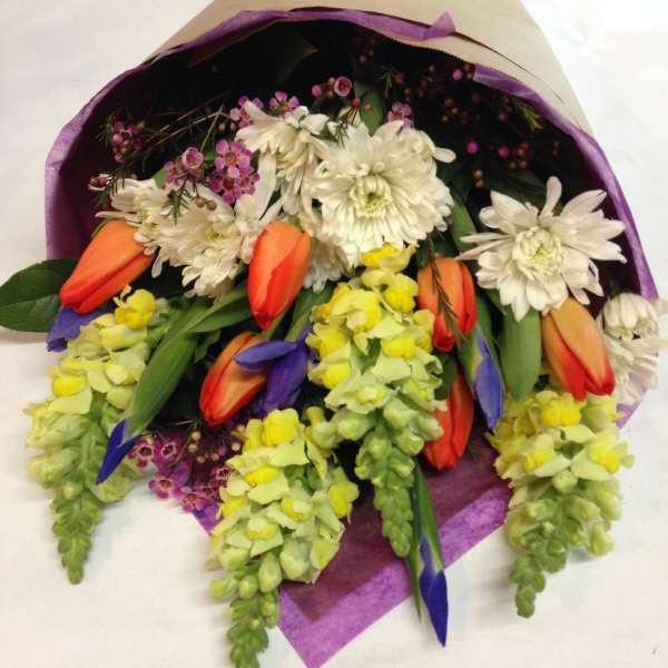 Bouquet of white daisies, orange tulips, and yellow snapdragons wrapped in purple paper