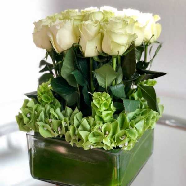 White roses arranged in a square glass vase with green hydrangeas