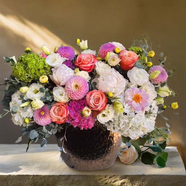 Mixed bouquet of pink, white, and purple flowers in a dark vase
