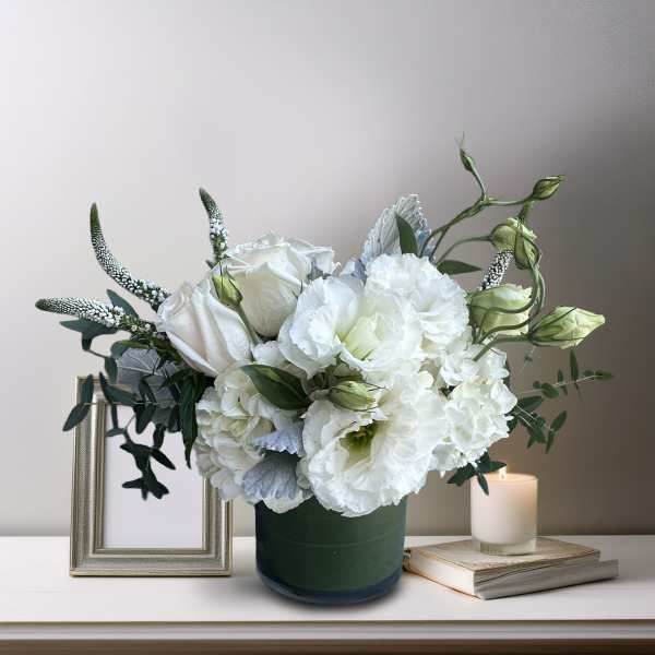 White floral arrangement in a green vase with a lit candle beside it