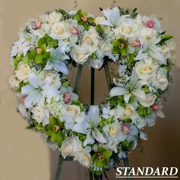 Heart-shaped standing wreath of white roses, lilies, and green orchids on an easel.