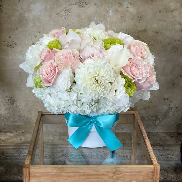 Pink and white flower arrangement in a white box with a blue ribbon