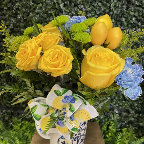 Yellow roses and blue carnations in a patterned mug with a bow
