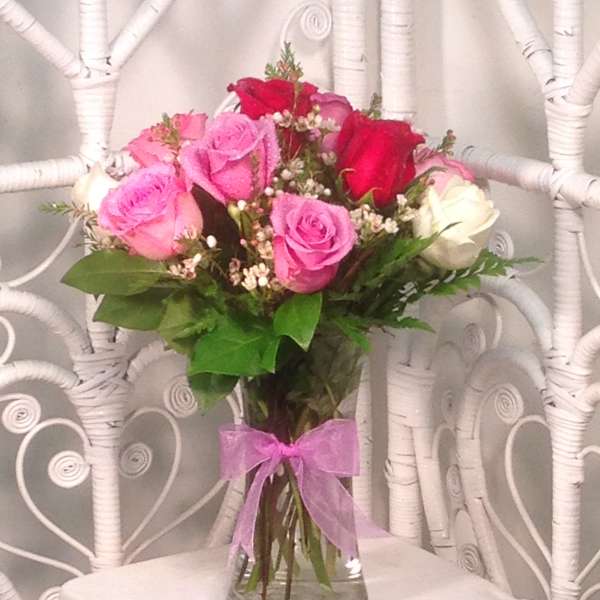Bouquet of pink, red, and white roses in a glass vase with a pink ribbon