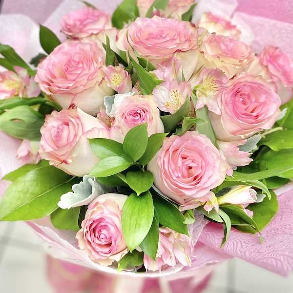 Hand-tied bouquet of pink roses and pale pink blooms wrapped in pink paper