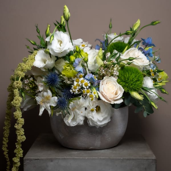 Mixed bouquet of white, blue, and green flowers in a gray vase