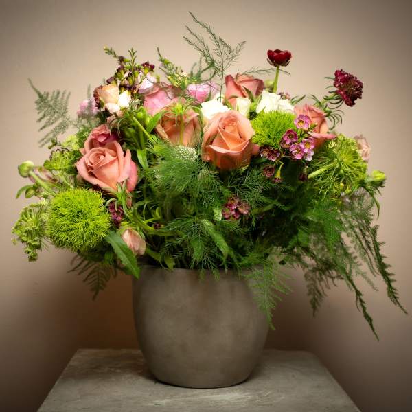 Lush peach rose and mixed flower arrangement with airy greenery in a gray ceramic pot