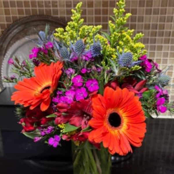 Bright mixed bouquet with orange gerbera daisies in a glass vase
