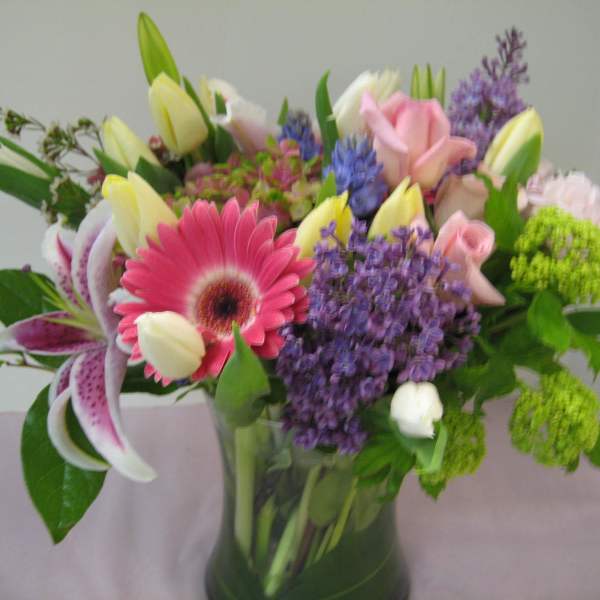 Mixed bouquet of pink gerbera, lilies, roses, tulips, and purple flowers in a clear glass vase