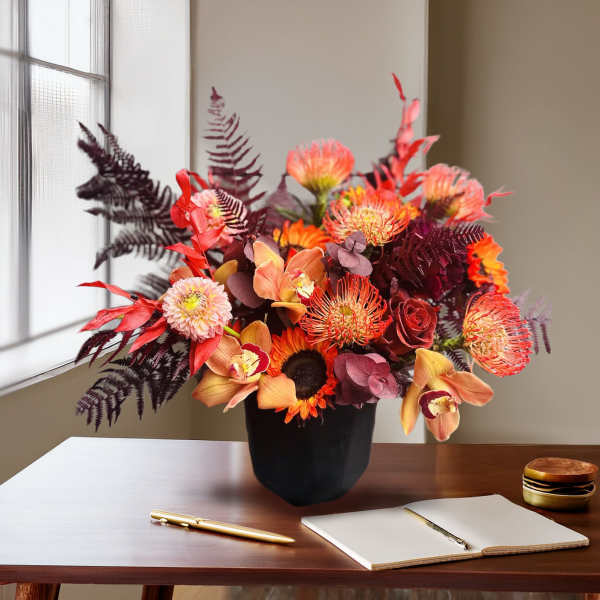 Orange and burgundy floral arrangement in a black vase on a desk